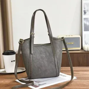 Borsa tote in pelle grigio scuro con tracolla su un tavolo in legno con caffè e riviste