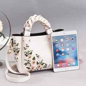 White leather shoulder bag with floral embroidery and braided handle next to tablet