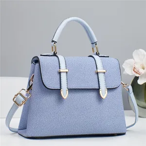 Chic light blue denim and leather handbag with gold hardware on a white pedestal