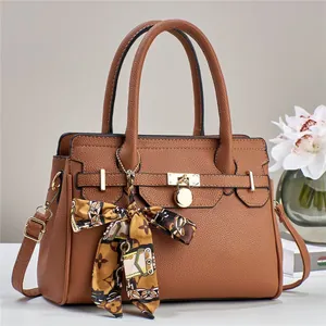 Dettaglio della borsa in pelle martellata con fibbie dorate e foulard in seta sul manico