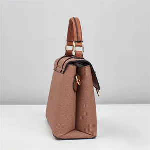 Detail view of brown textured tote bag showing side trapezoidal structure and gold hardware