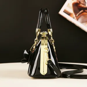Detail view of glossy black patent leather shell bag with gold metal frame and floral charm