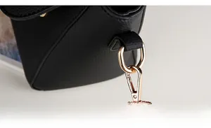 Macro view of black litchi grain leather bag with light gold D-ring and metal hook details