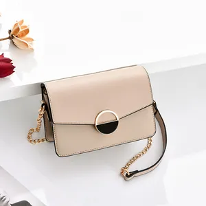 Piccola borsa a tracolla beige minimalista con catena dorata su sfondo bianco