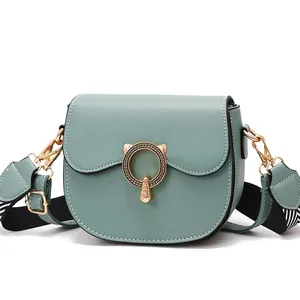 Stylish sage green saddle bag with wide striped strap and cat-ear gold buckle design