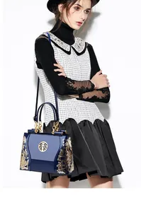 Detail of navy blue patent leather handbag with golden floral embroidery and metallic ornament