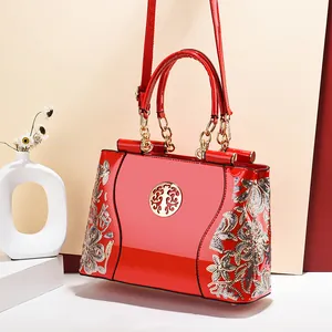Red patent leather handbag with floral embroidery and golden chain handle shown from a side view