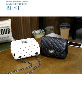 Detail of quilted crossbody bags with silver chain straps and metal rivets on wooden table