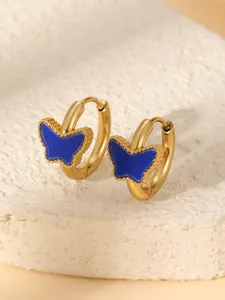Détail de créoles dorées avec papillon en émail bleu posées sur un support en pierre