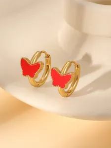 Détail de boucles d'oreilles créoles papillon dorées avec incrustation rouge sur céramique