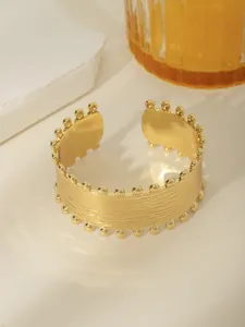 Dettaglio del bracciale rigido largo placcato oro 18k con texture spazzolata e bordi perlati