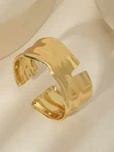 Dettaglio di un bracciale rigido placcato oro 18k con texture a onde e finitura lucida