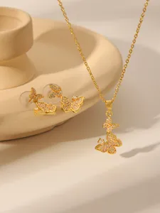 Detailopname van gouden vlinder ketting en oorknopjes met zirkonia op een keramiek blad