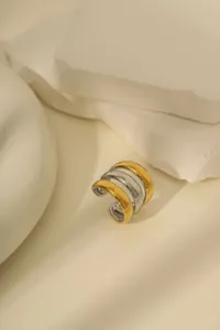Detail von geschichtetem Ear Cuff in Gold und Silber auf weißem Stein mit Schatten