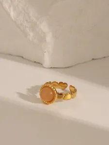 Detail of peach stone ring with heart-shaped gold band on white textured rock