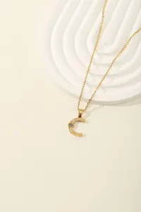 Detail of gold letter C pendant with blue stone and crystals on white geometric stand