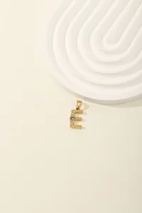 Close-up of golden letter E pendant with blue and white zircon stones and sunburst texture