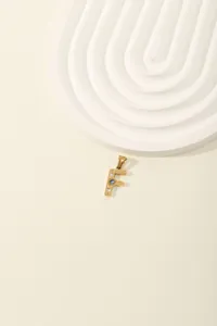 Detail of gold letter F pendant with blue zircon inlay and engraved radial texture