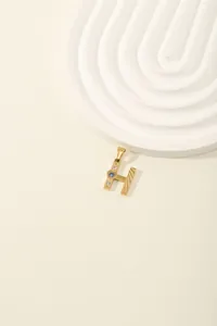 Detail of golden H letter pendant with blue and white crystals on beige background