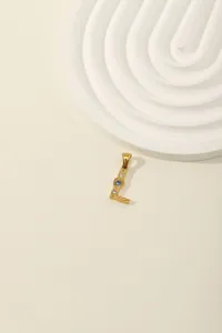 Detailed view of a gold letter L pendant with blue and white zircon stones on a beige background