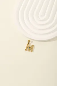 Detail of gold letter M pendant with blue gemstone and cubic zirconia accents