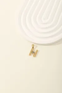 Detail of gold letter N pendant with blue gemstone and diamonds on textured metal