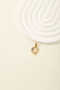 Detail of gold letter Q pendant with blue zircon stones and brushed metal texture