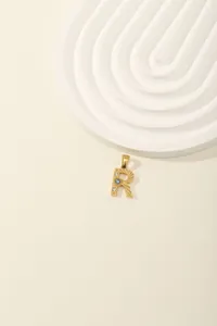 Macro view of a gold-plated letter R pendant with blue and white zircons on white steps