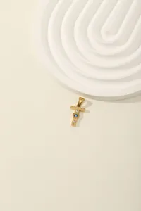 Detail of a gold cross pendant with radiant texture and inlaid blue and white zircons