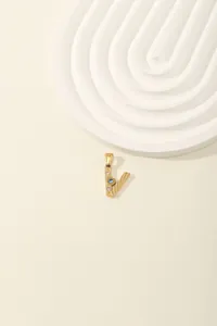 Macro detail of gold V-letter pendant with light blue gemstone and zircon inlay
