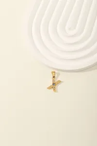 Detailed macro of a gold letter X pendant featuring a blue center stone and zircon accents