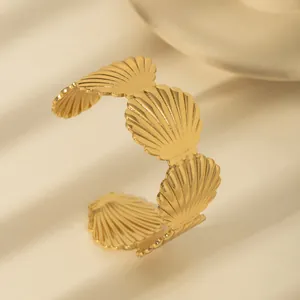 Macro detail of a golden C-shaped open bangle featuring textured shell-shaped design elements