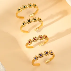 Detail of four adjustable flower rings in gold with green, red, blue, and black stones