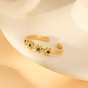 Detail of gold open ring featuring green zircon-set floral petals on a warm sandy base