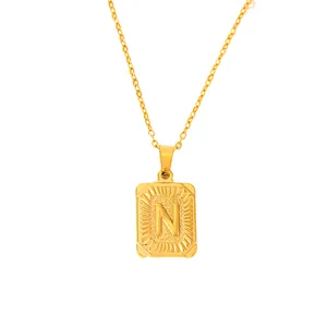 Macro detail of gold-plated rectangular pendant featuring an embossed letter N design