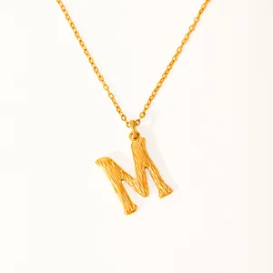 Detail of 18k gold plated letter M pendant with textured surface and fine link chain