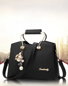 Detail of black pebbled leather handbag featuring golden metal handles and floral bag charm