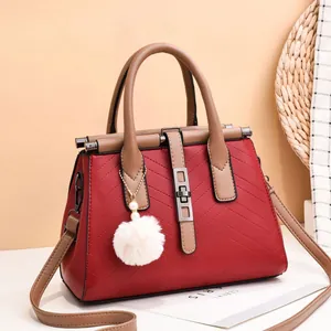 Deep red quilted handbag with khaki handles and pearl fur ball charm, crossbody view