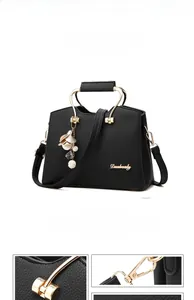 Close-up of black litchi grain leather bag with golden metal handles and pearl charms