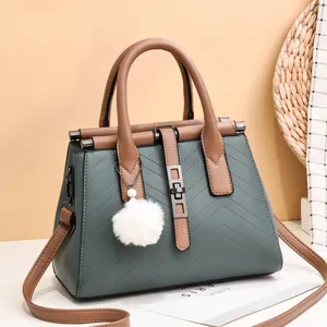 Green and brown crossbody bag with V-shaped quilting and a fuzzy pom-pom charm