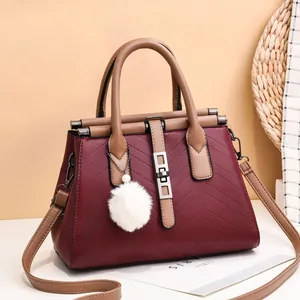 Detail of burgundy quilted leather handbag with brown handles and a fluffy white charm