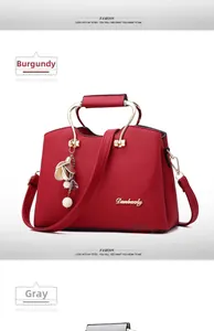 Detail view of wine red tote bag with metal handles and decorative flower pearl charm