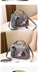 Detail of grey crossbody bag with 3D floral accents and fuzzy ball charm on marble