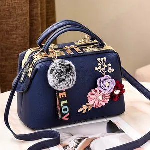 Navy blue faux leather handbag with floral accents and pompom keychain on marble