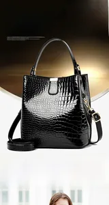 Detail of glossy black crocodile embossed bucket bag with gold hardware and strap