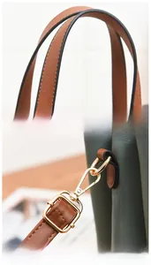 Detail of green PU leather handbag featuring brown handles and gold-tone metal hooks