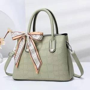 Detail of mint green crocodile embossed tote bag featuring elegant silk scarf handle decoration