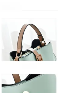 Detail of mint green handbag with brown leather handle and gold zipper closure