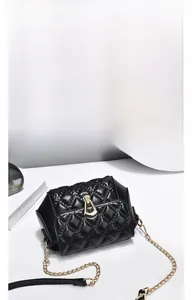 Detail of black quilted chain bag with elegant gold geometric metal lock and leather strap