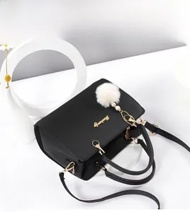 Detail of black faux leather handbag with golden hardware and white plush charm